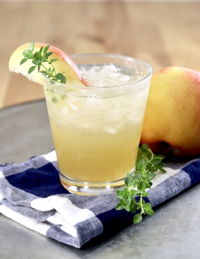 Apple Cider Gin Cocktail in a small glass on a tray. Garnished with apple slice and fresh thyme