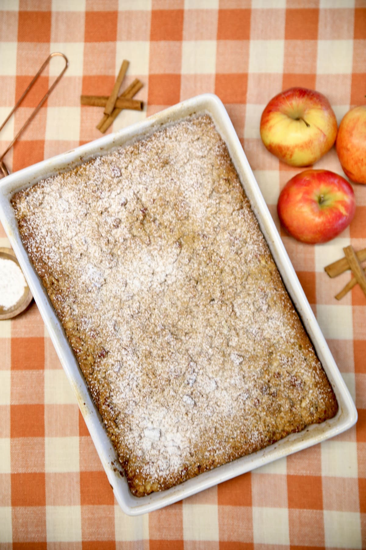 Apple streusel coffee cake on checked table cloth, apples and cinnamon sticks. 