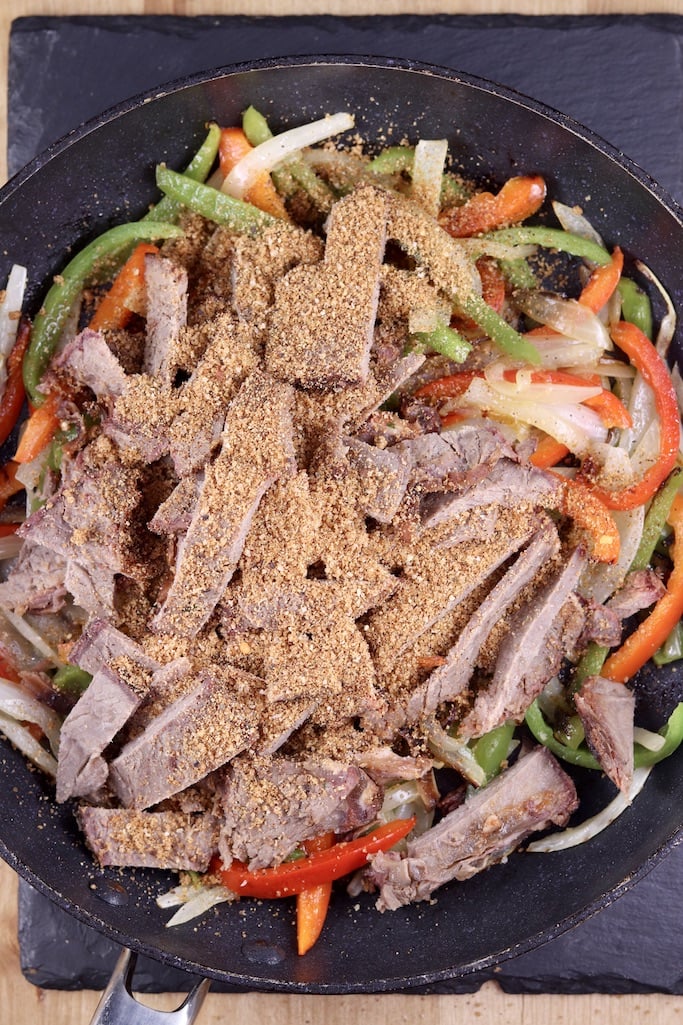 skillet of peppers and onions topped with roast beef and dry rub seasonings