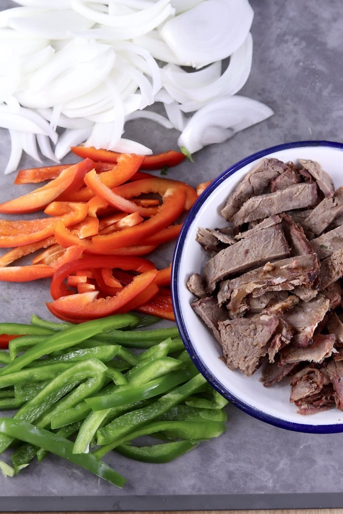Sliced onions, red & green bell peppers, bowl of sliced roast beef