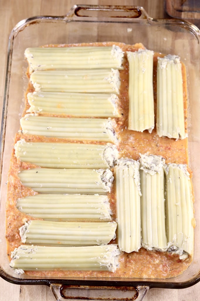 Stuffed manicotti shells in a baking dish over creamy tomato sauce