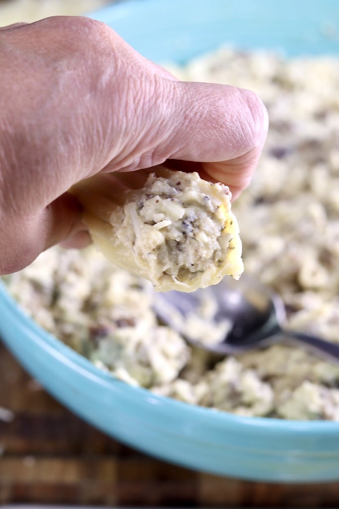 hand holding manicotti shell stuffed with sausage and cheese