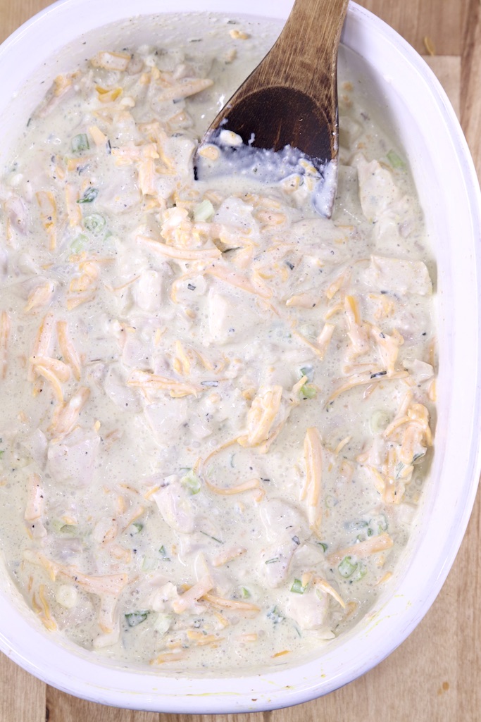 Casserole dish with chicken, cheese and creamy sauce with wood spoon