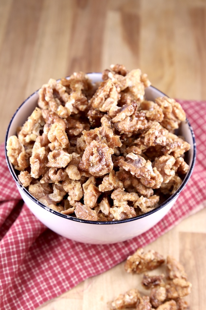 Candied Walnuts in a white bowl on a red check napkin, a few walnuts on the wood table