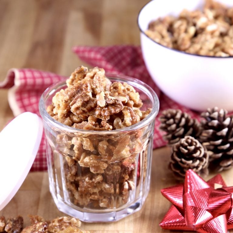 Candied Walnuts in a small jar for a gift, pine cones and red bow with a white bowl of walnuts