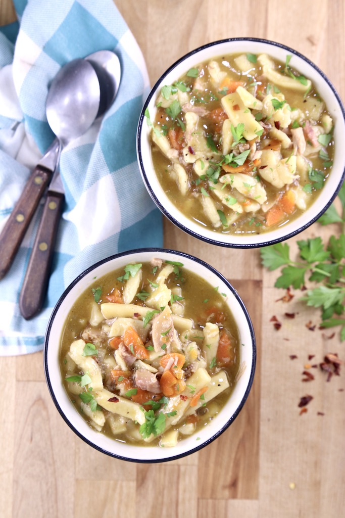 2 bowls of turkey noodle soup with spoons and a blue napkin