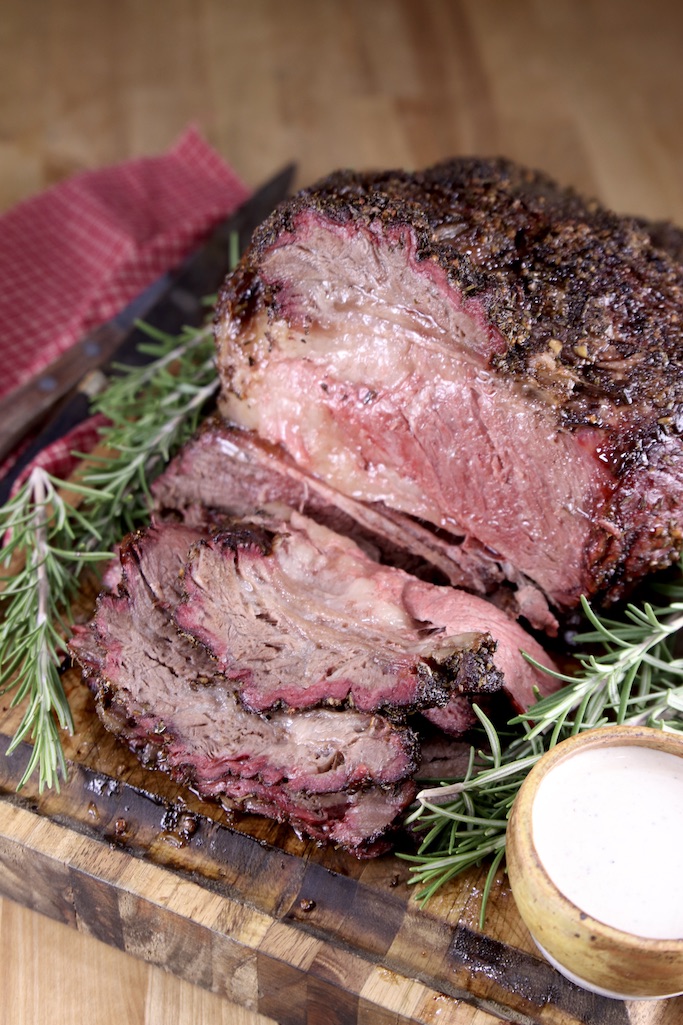 Sliced prime rib roast with rosemary garnish and small bowl of horseradish sauce