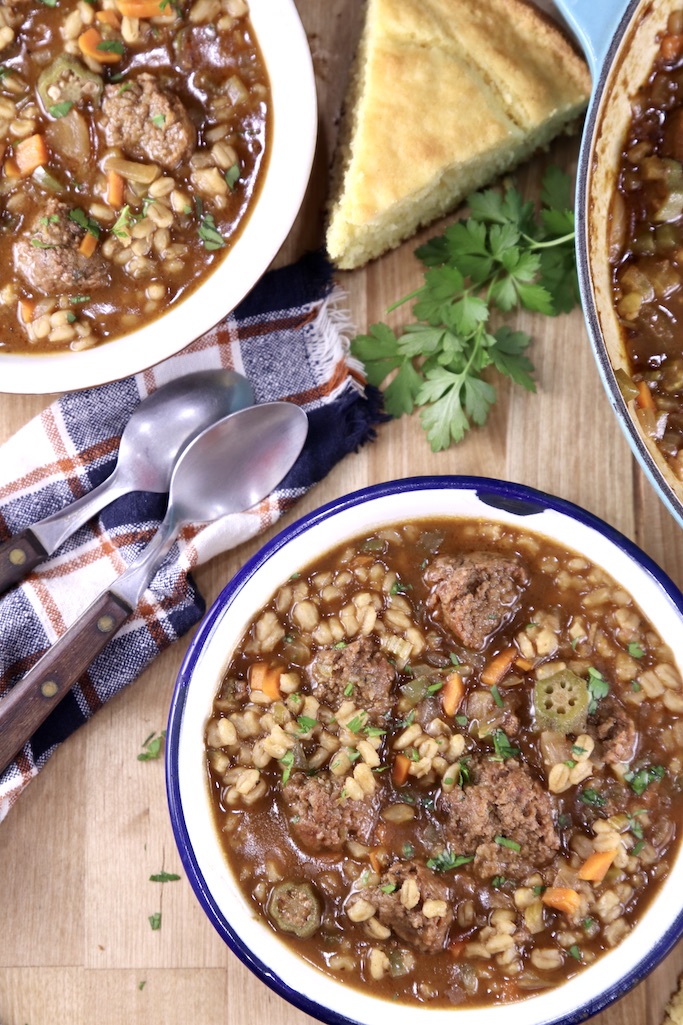 smoked sausage barley soup in 2 bowls with a slice of cornbread and parsley