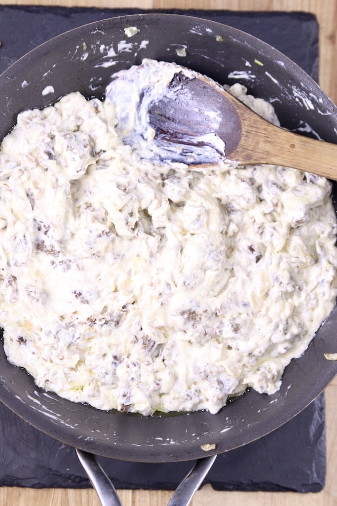 cream cheese and sausage filling for mushrooms in a skillet with a wood spoon