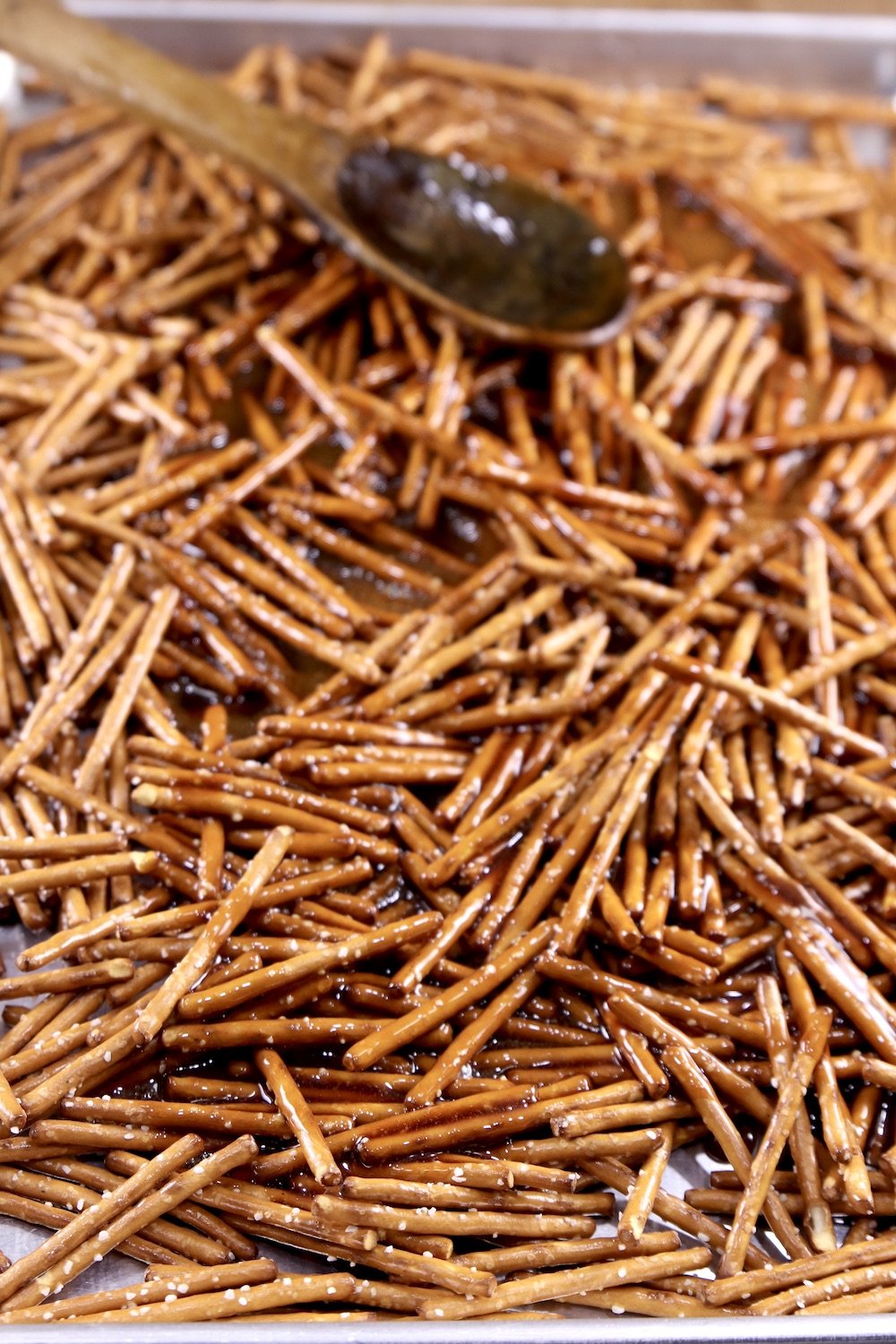 stirring candied pretzels on a sheet pan with a wood spoon