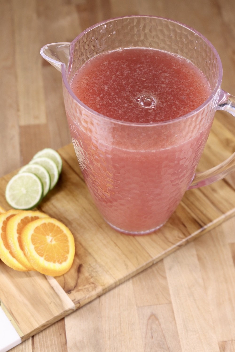 Pitcher of Christmas punch on a wood board with slices of orange and limes.