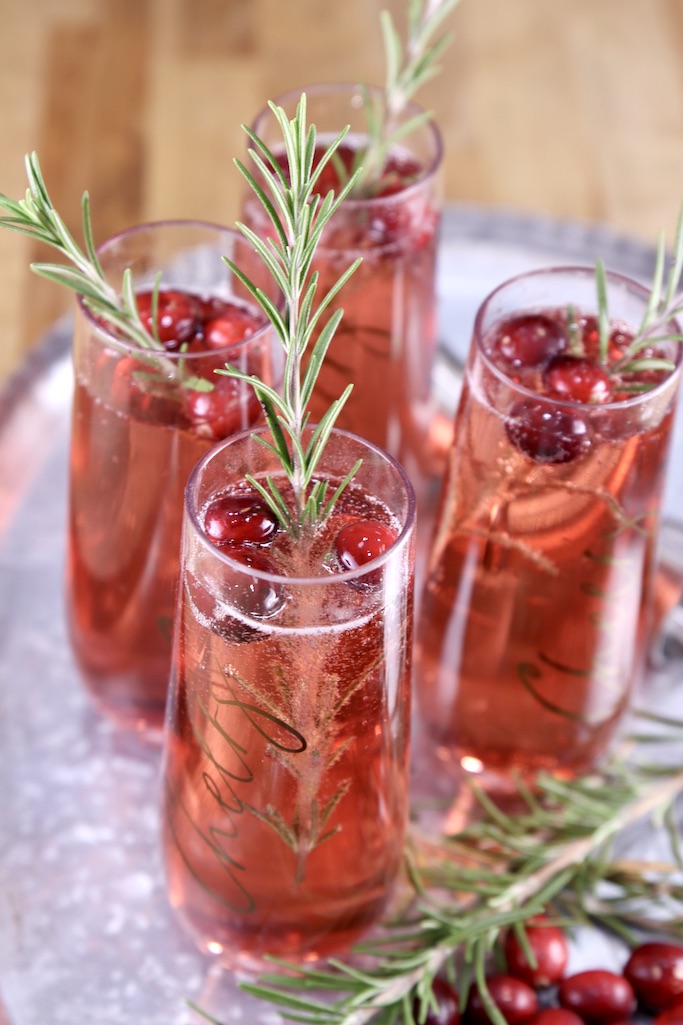 Mimosa Cocktails in stemless champagne flutes on a tray with cranberry and rosemary garnish