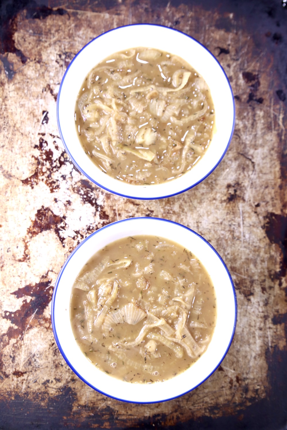 2 bowls of French Onion soup on a seasoned baking sheet