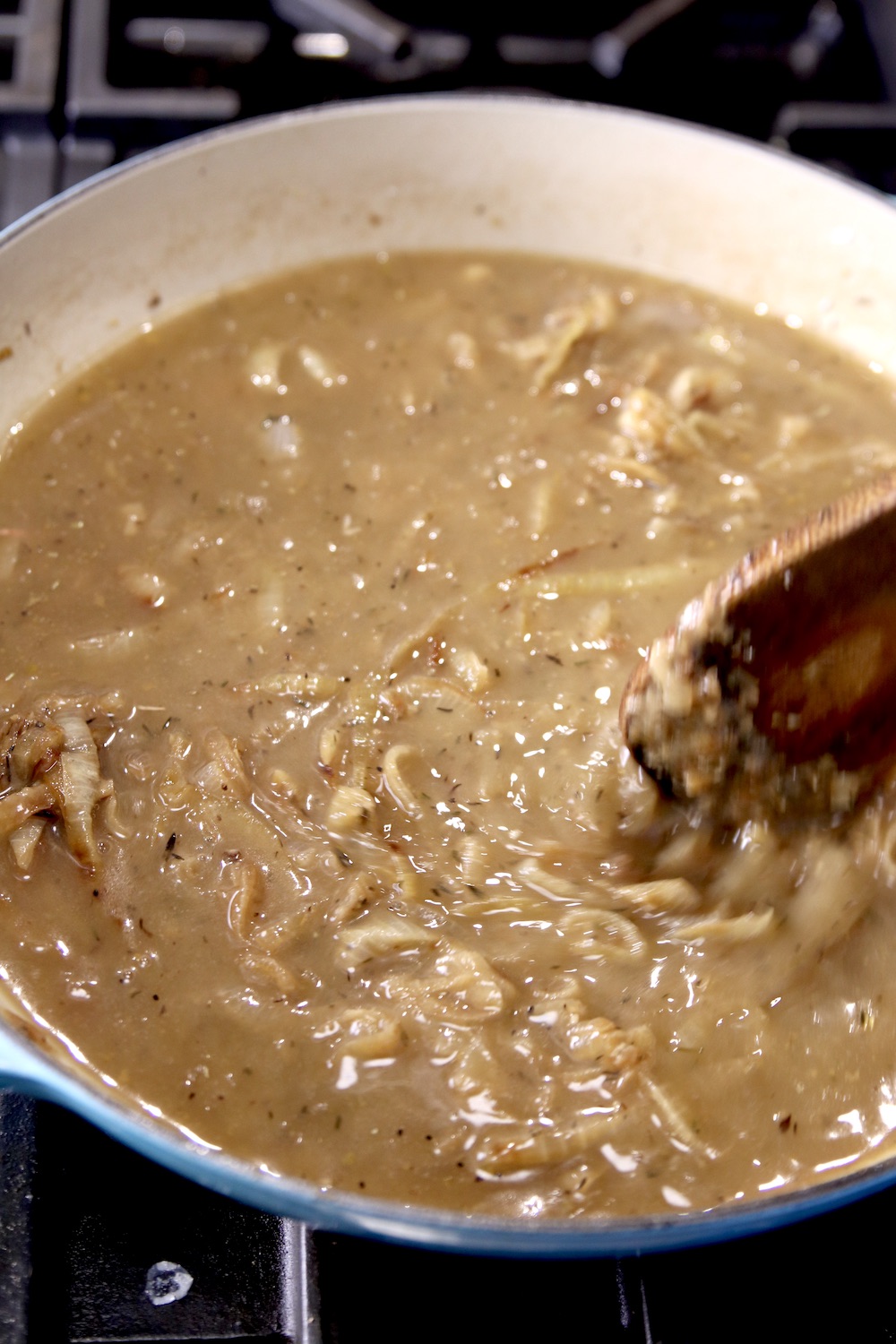 Spoon stirring French onion soup in a pan