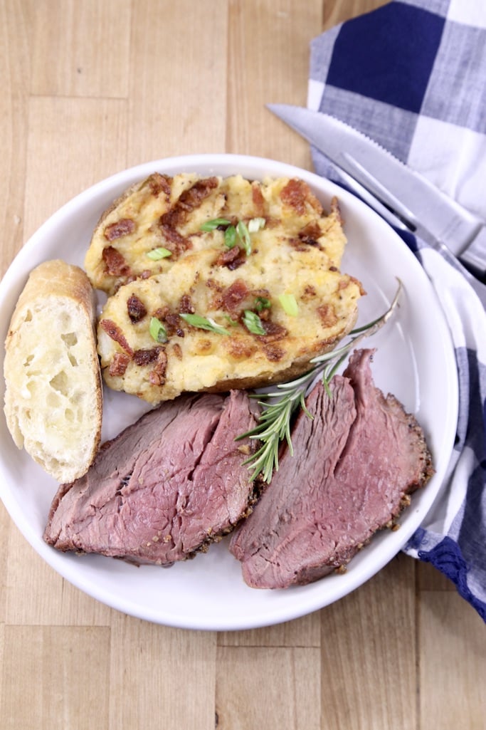 Beef tenderloin slices on a plate with bread and twice baked potato