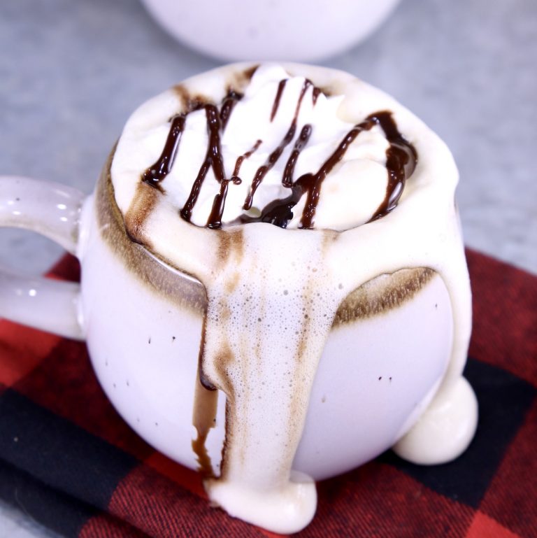 Mudslide Coffee with whipped cream and chocolate drizzle, dripping over the mug onto the red check napkin