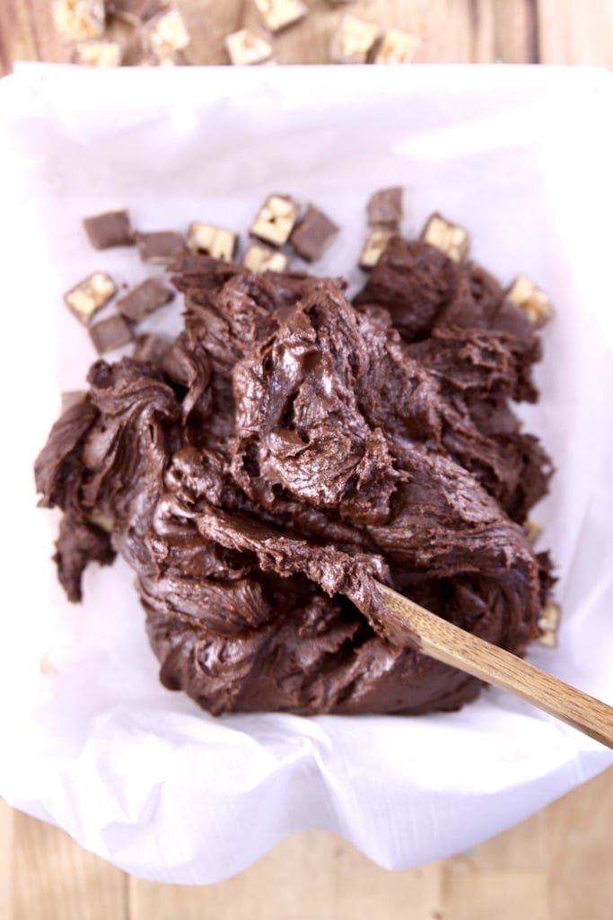 Pouring fudge mixture over mini snickers bars in a lined pan
