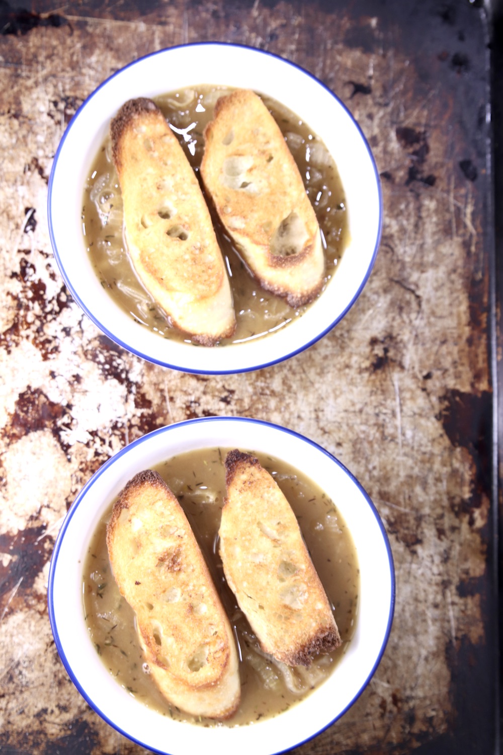 Two bowls of French Onion Soup topped with 2 slices of baguette on a baking sheet