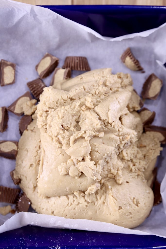 Peanut butter fudge poured over parchment paper with chopped mini peanut butter cups