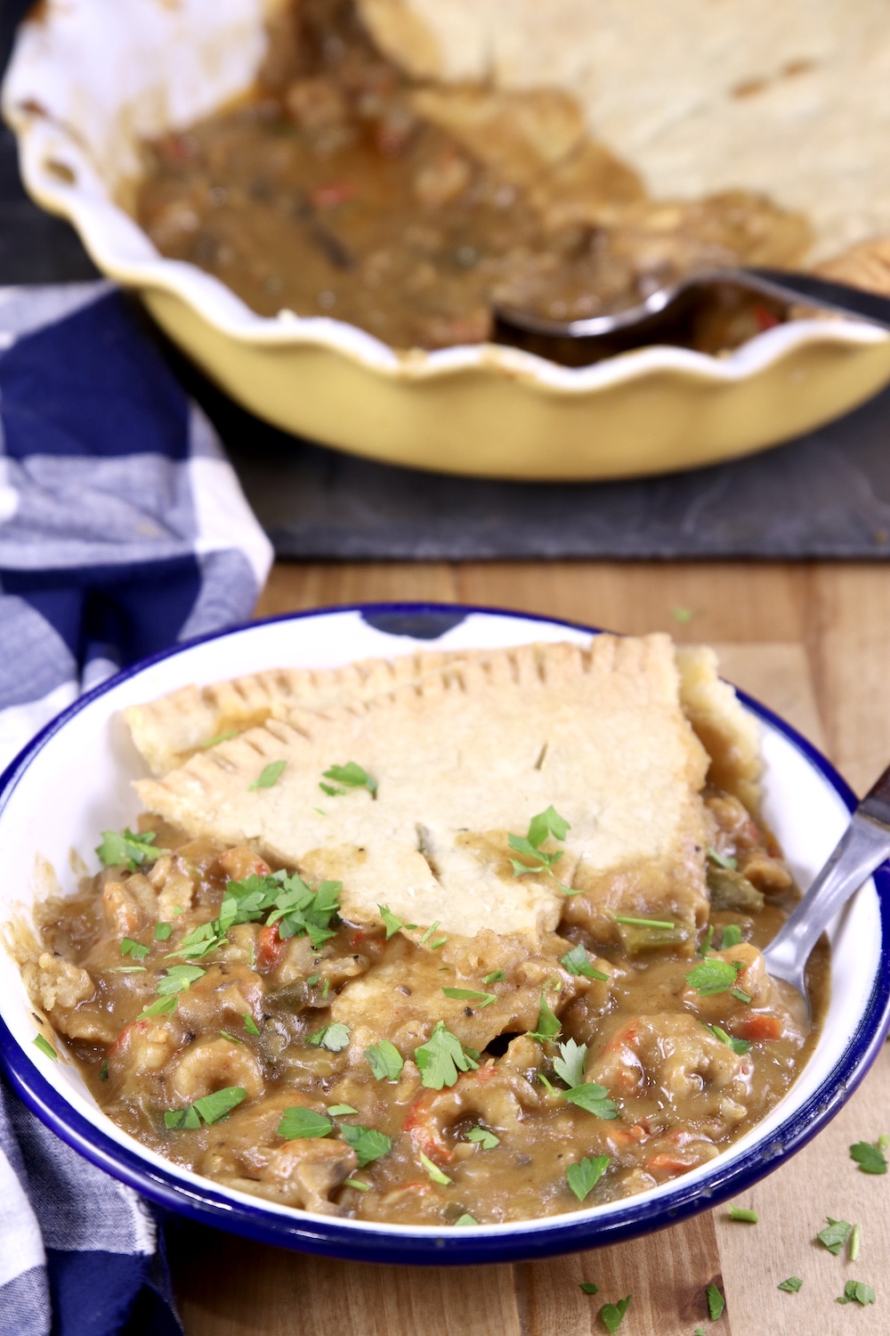 Bowl of crawfish pie with a spoon, pie plate in background