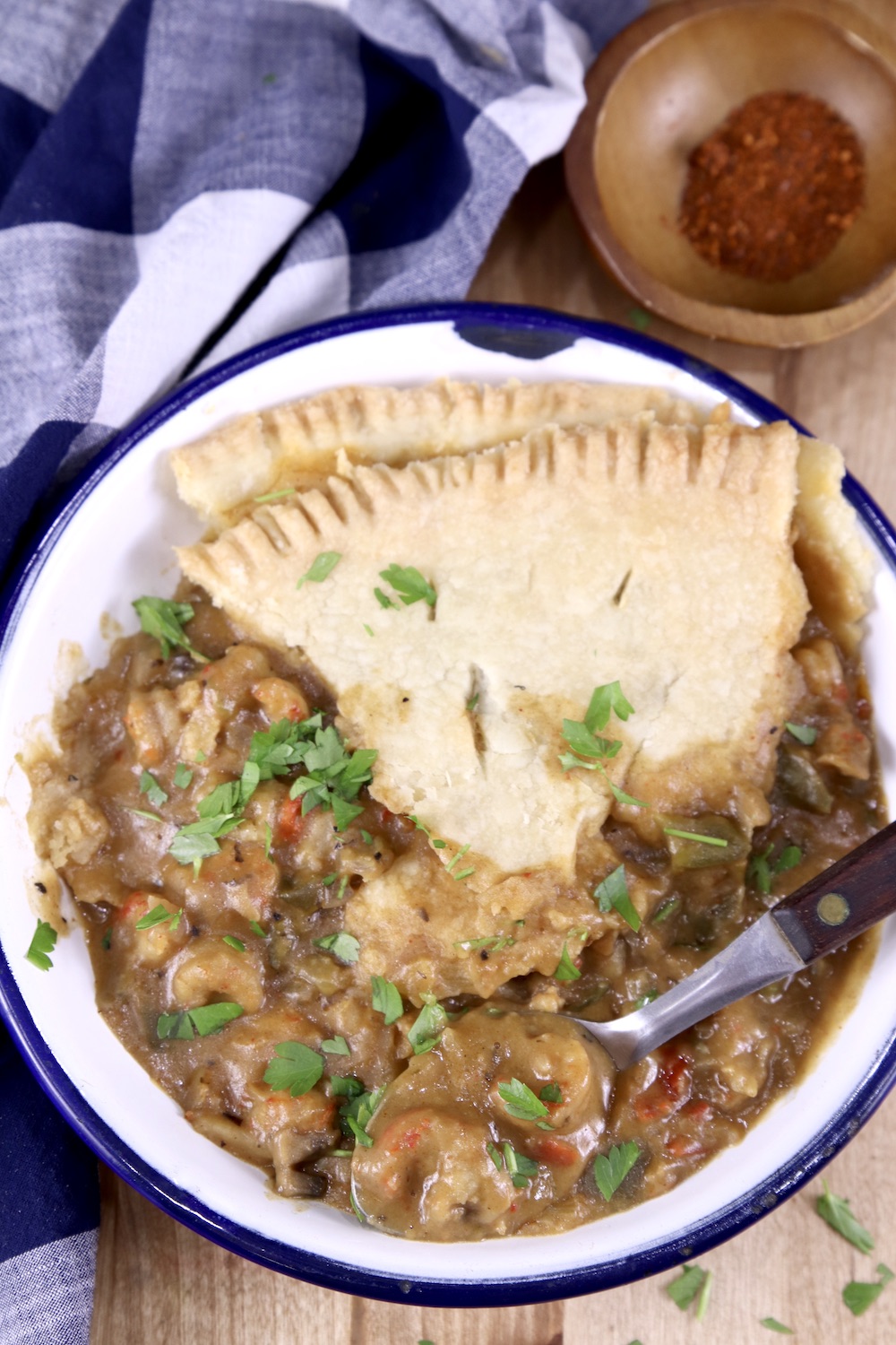 Bowl of crawfish pie with blue and white napkin, spoon in bowl