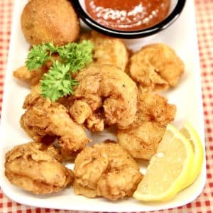 Fried shrimp on a plate with lemon wedges, parsley and cocktail sauce.