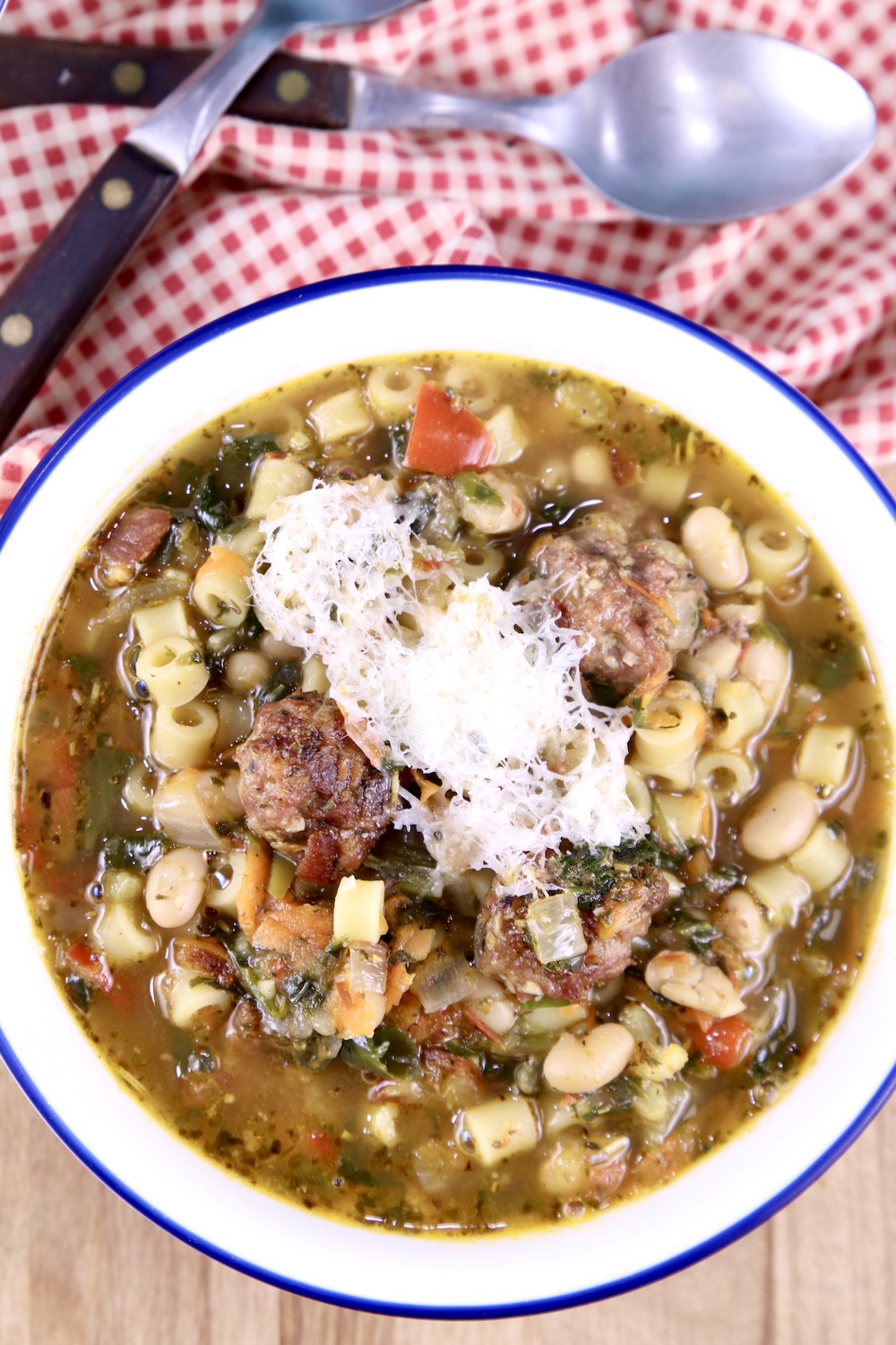 Meatball Soup with parmesan cheese grated over the top, spoons, red check napkin
