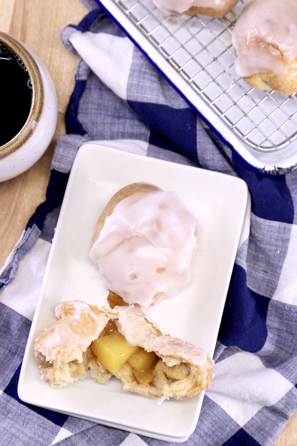 plate of peach cobbler dessert bombs, one split in half, cup of coffee, tray of desserts in background
