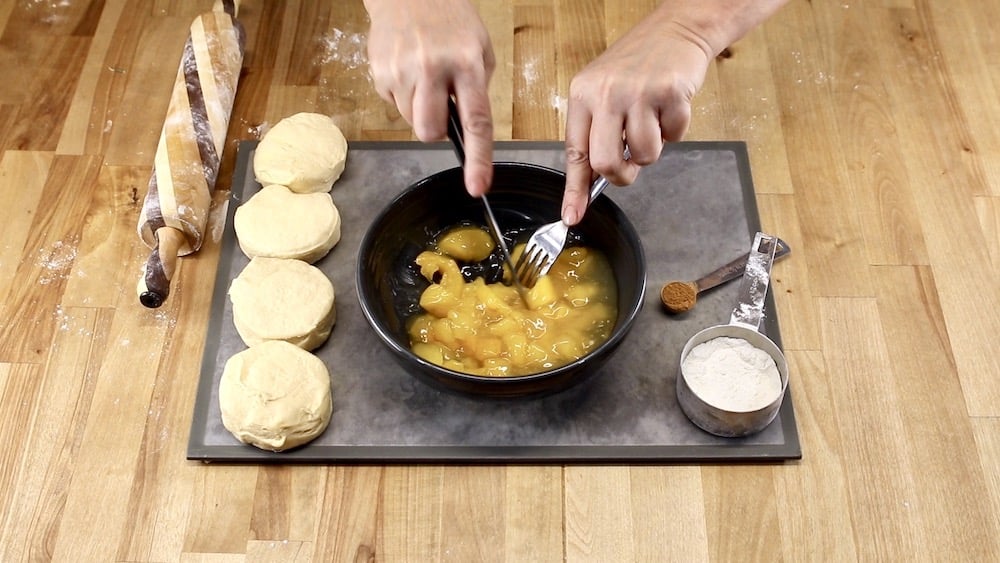 peach pie filling in a bowl, using a knife and fork to chop slices