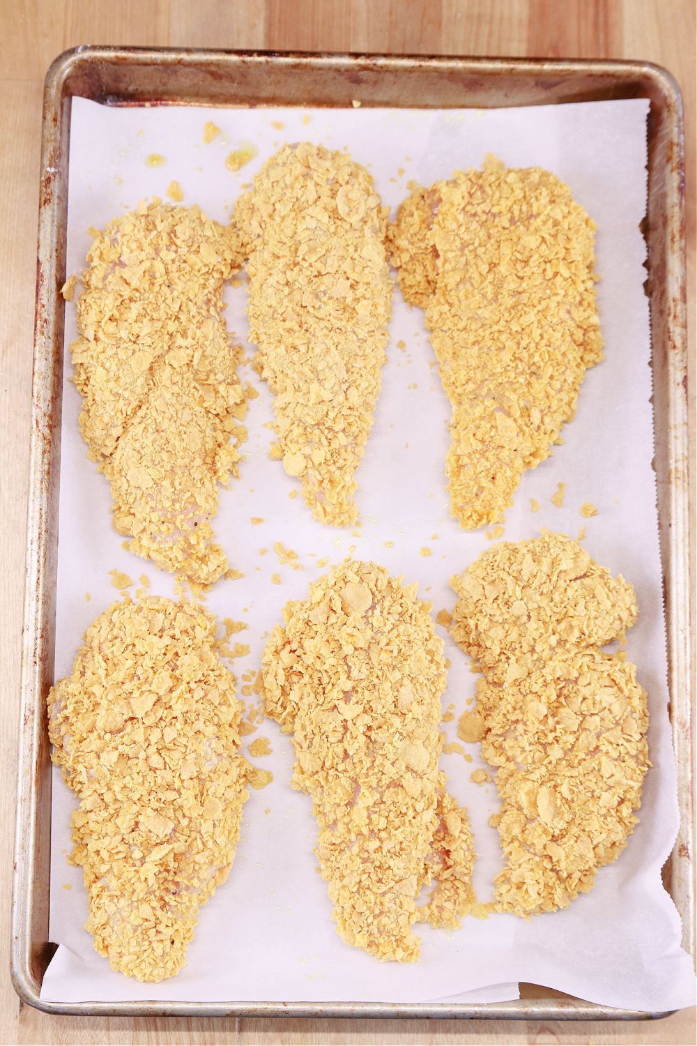 Parchment lined baking sheet with cornflake coated chicken