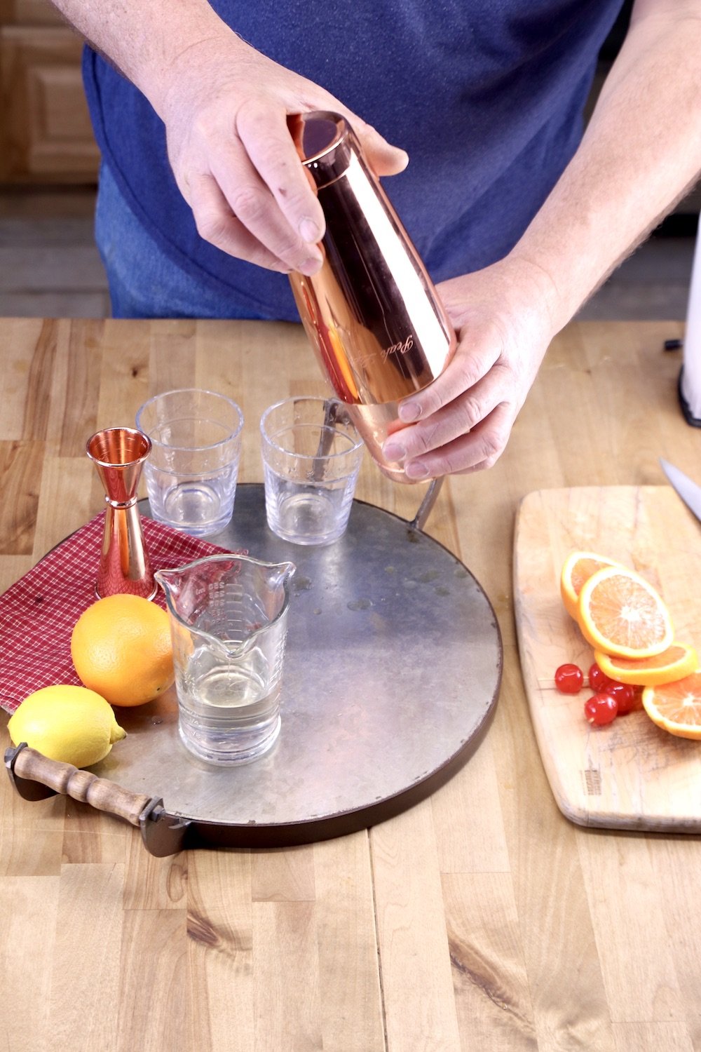 man shaking cocktail over tray of glasses with whole lemon and orange and glasses
