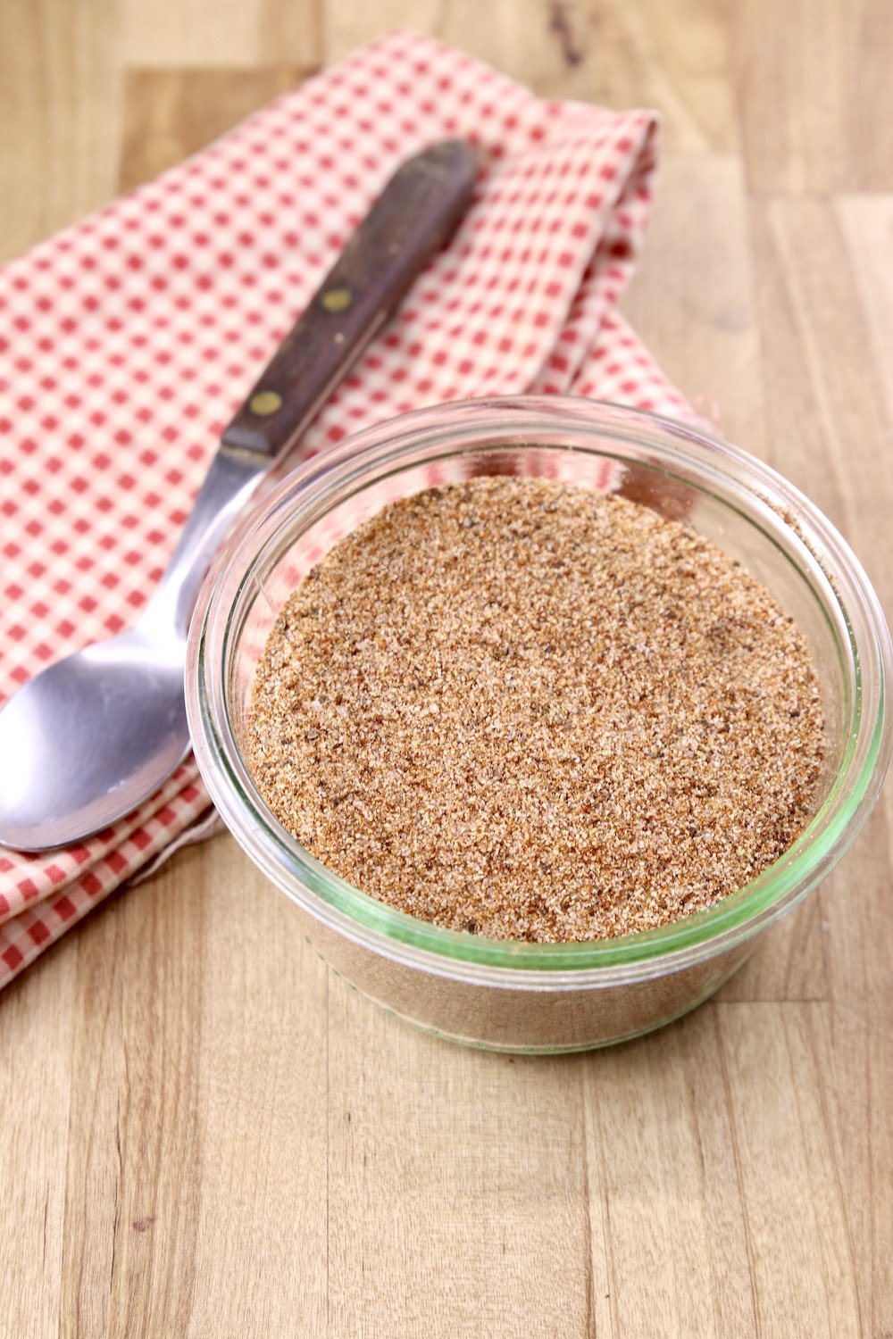Homemade Chili Seasoning in a glass jar, spoon on a red napkin