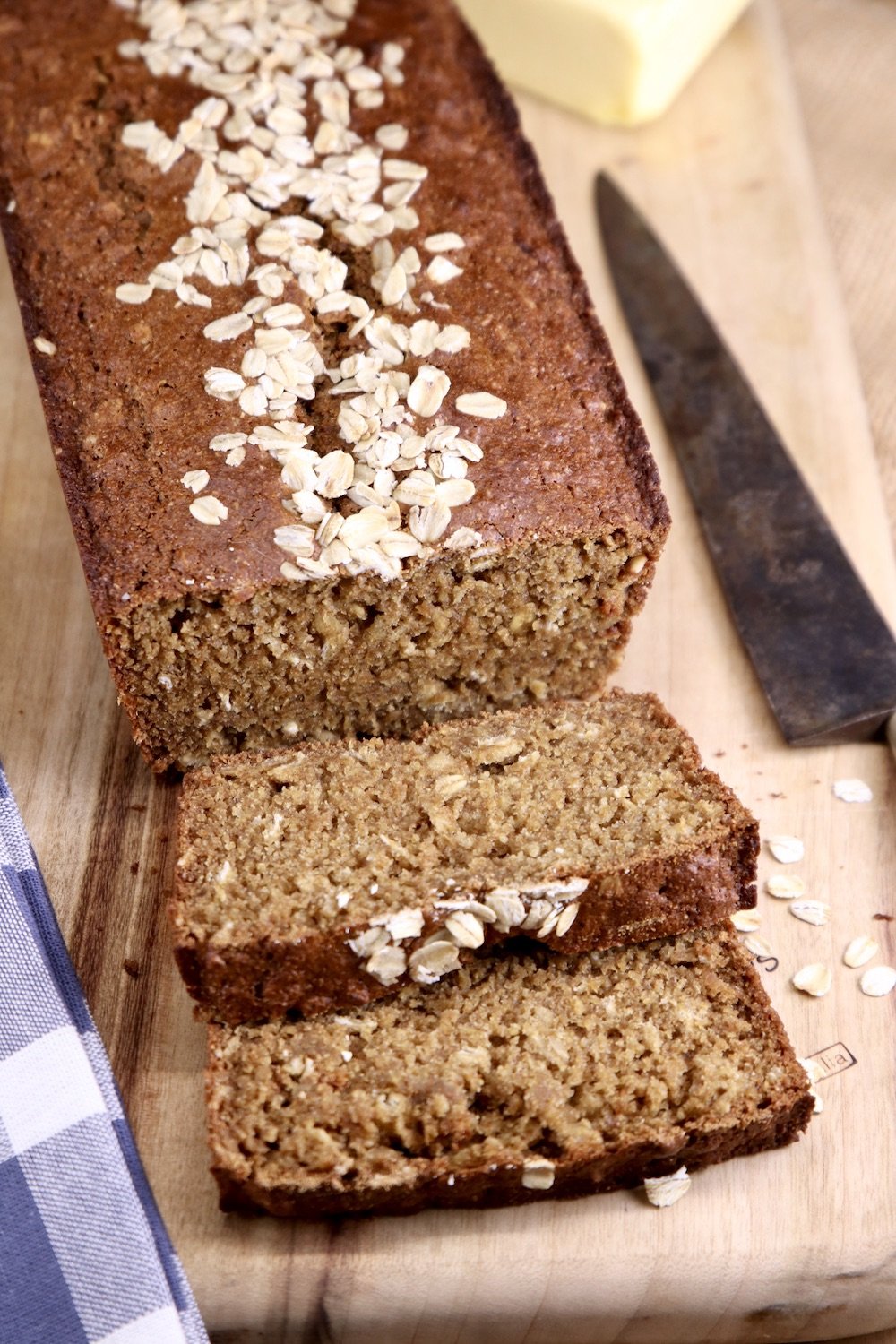 cutting board and knife with loaf of sliced brown bread with oat topping