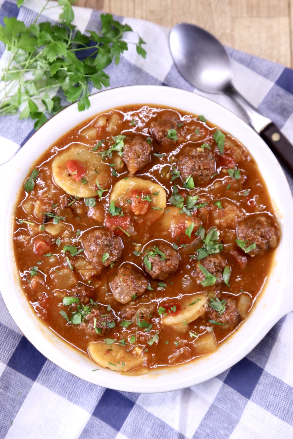 Meatball Soup with bunch of parsley sitting on a blue and white check napkin