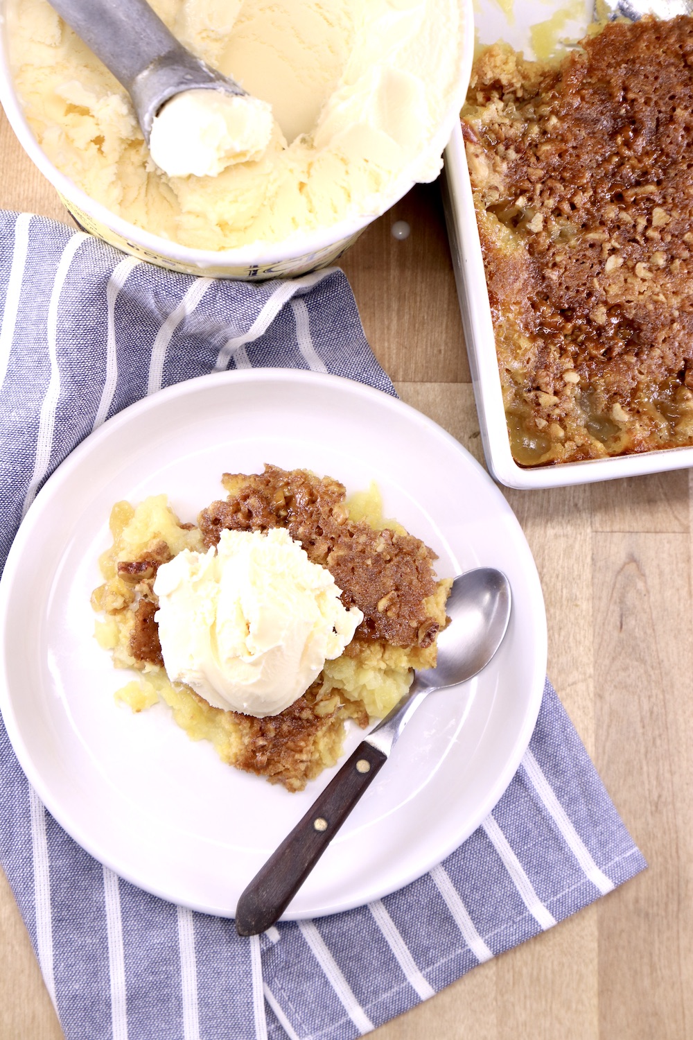 Pineapple Dump Cake served with vanilla ice cream. Cake pan & ice cream carton above the plate
