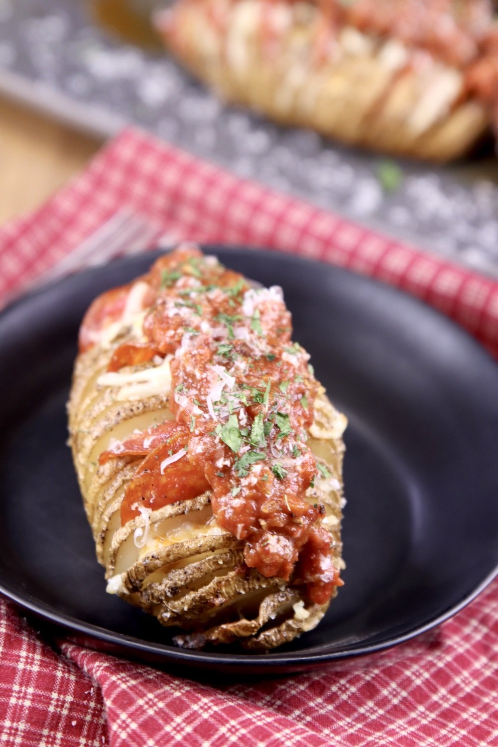Hasselback Potato topped with pizza sauce and cheese on a black plate