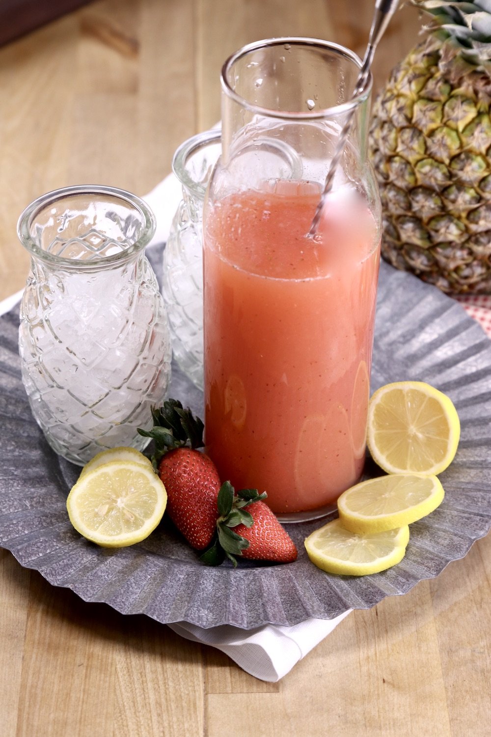 pitcher of strawberry lemonade cocktail on a platter with glasses and fresh fruit garnishes