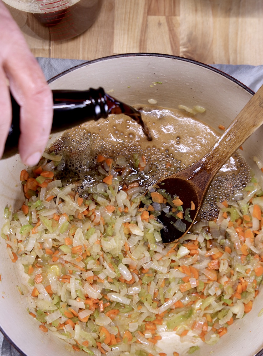 Pouring stout into pan of cooked vegetables for beef stew
