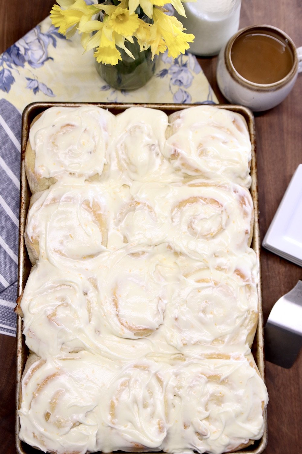 Pineapple Sweet Rolls in a pan on a table with yellow flowers and a cup of coffee