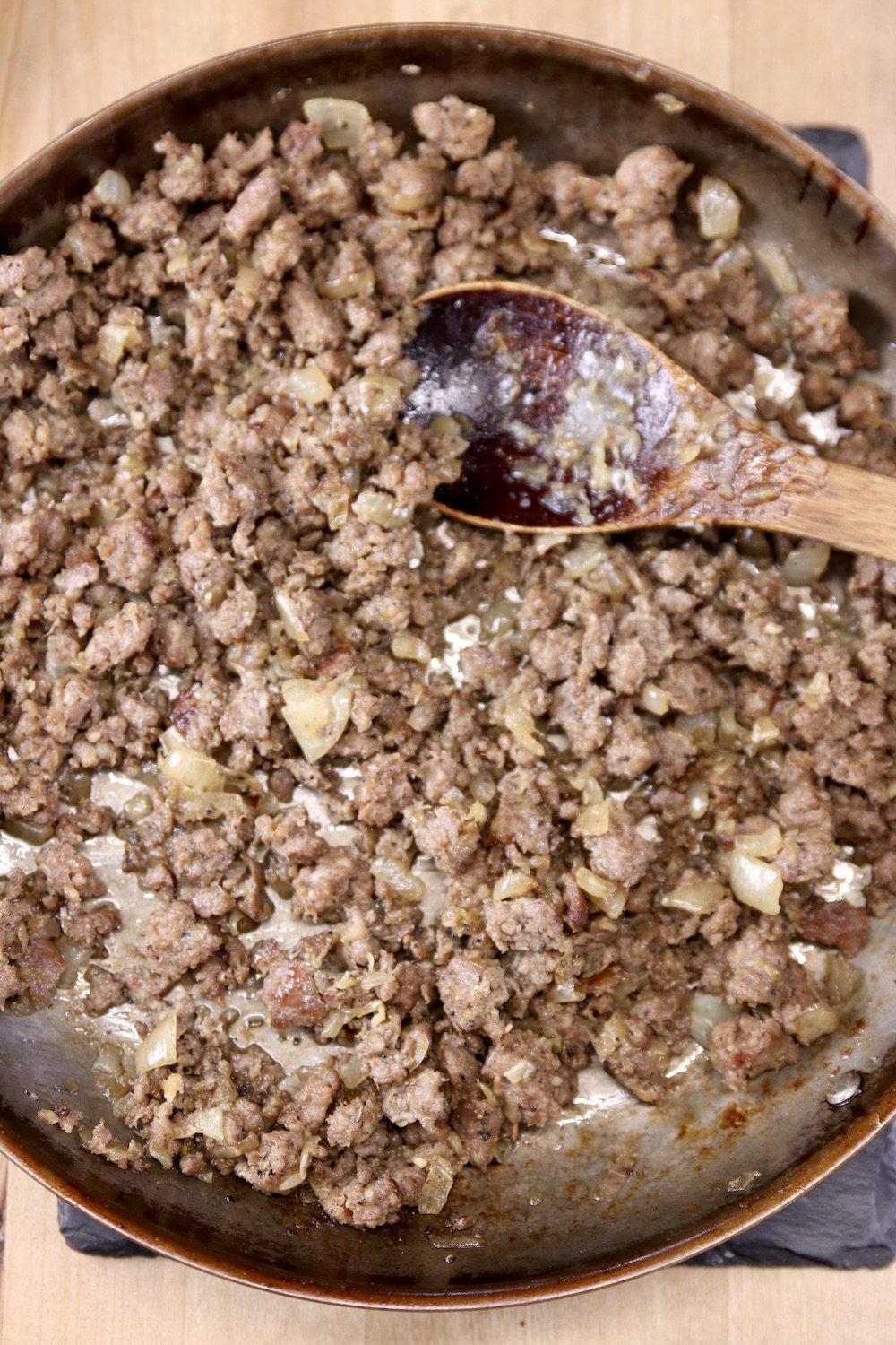 skillet of browned sausage with a wood spoon