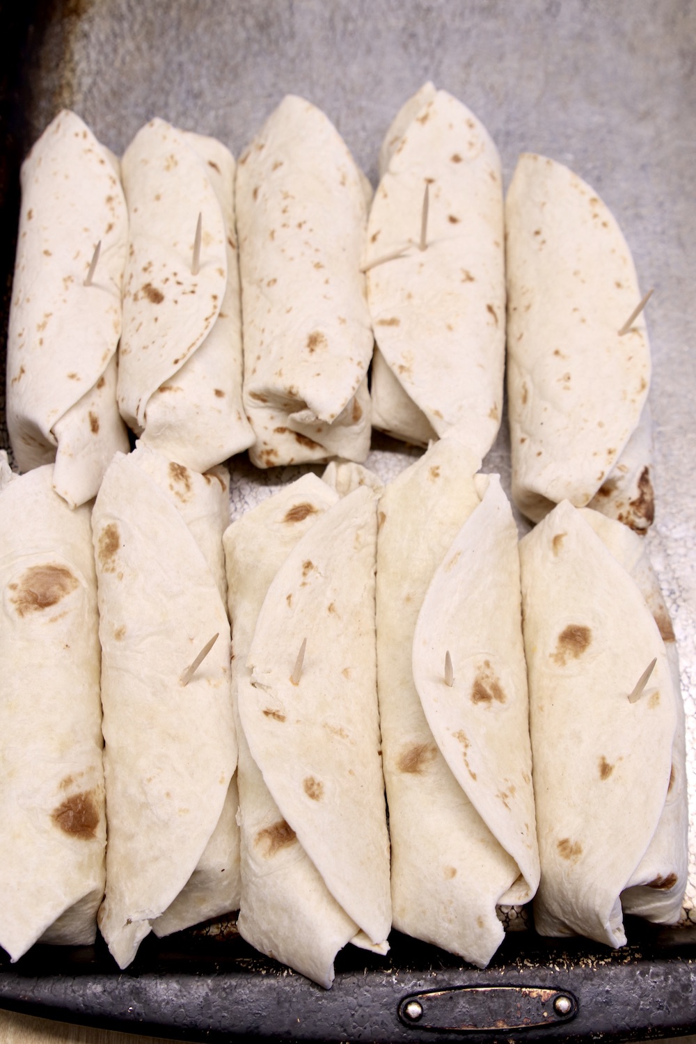 Beef burritos on a sheet pan secured with toothpicks