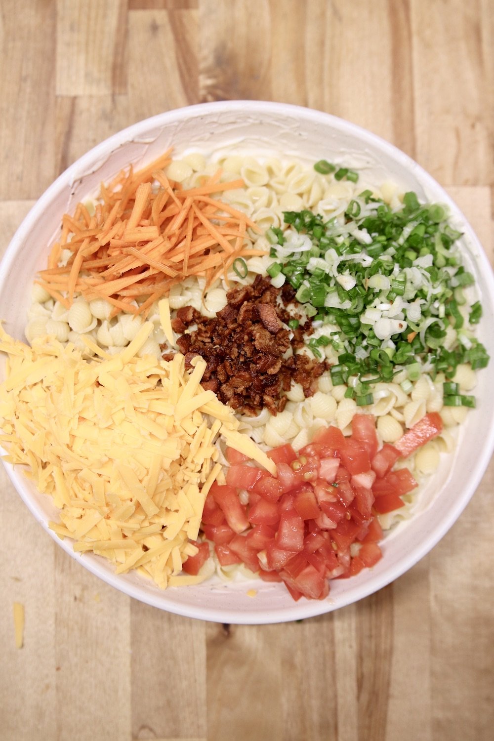 bowl of pasta with carrots, cheese, green onions, bacon and tomatoes