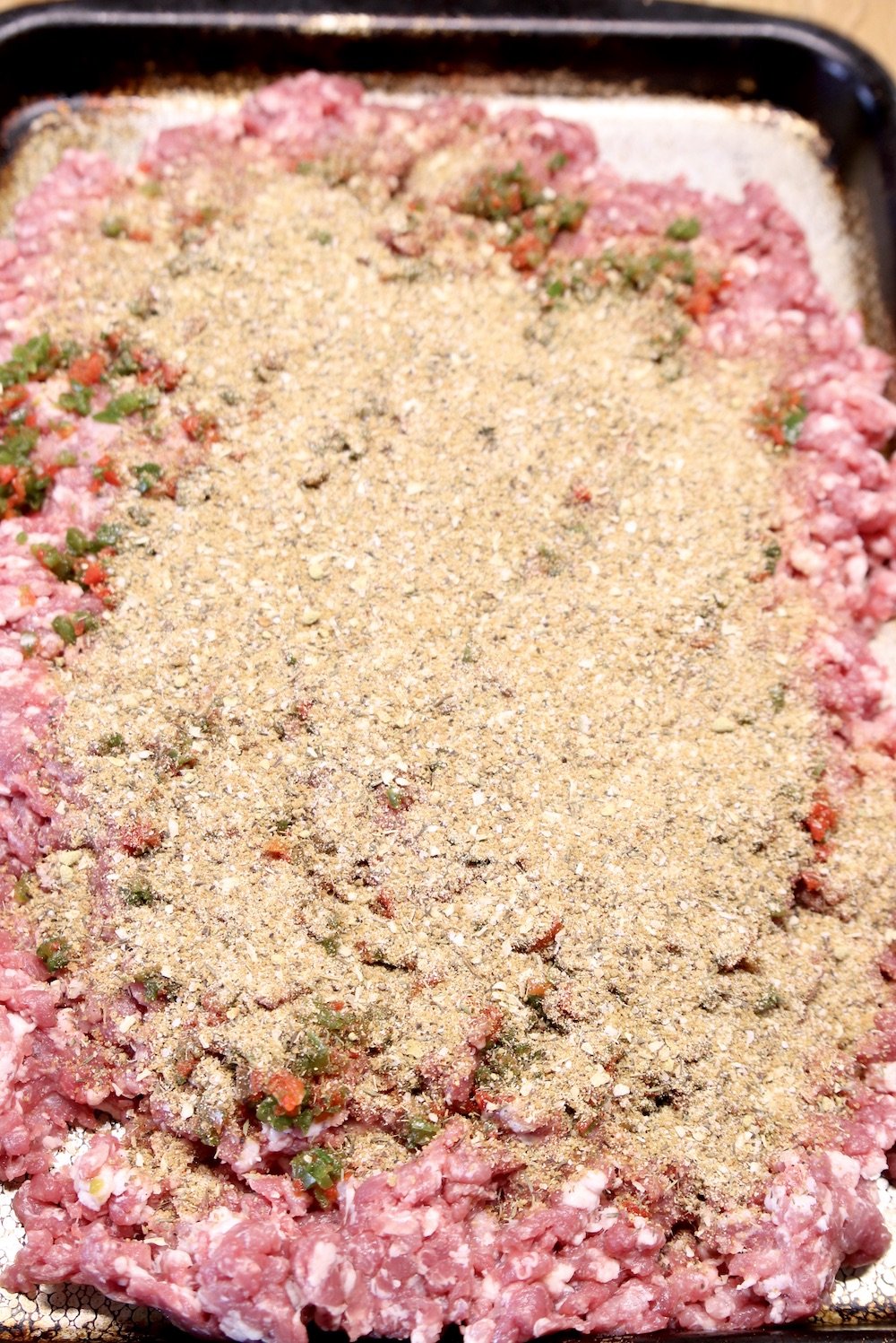 spices and brown sugar sprinkled over pan of ground pork for sausage