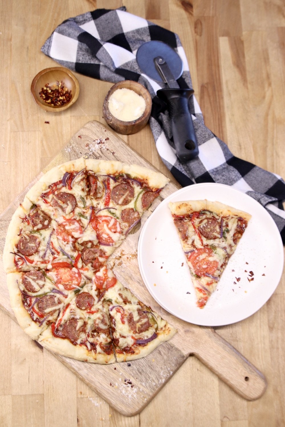 Smoked Sausage Pizza on a cutting board with one slice on a plate