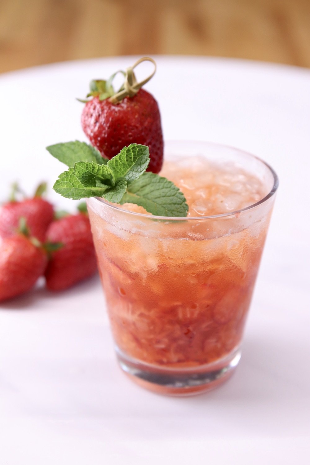 TX Kiss strawberry whiskey cocktail with mint and strawberry garnish on a white serving tray