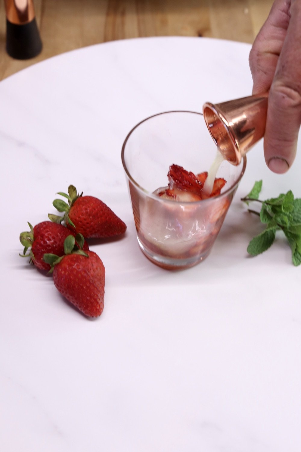 pouring lemon juice into cocktail glass with a copper jigger