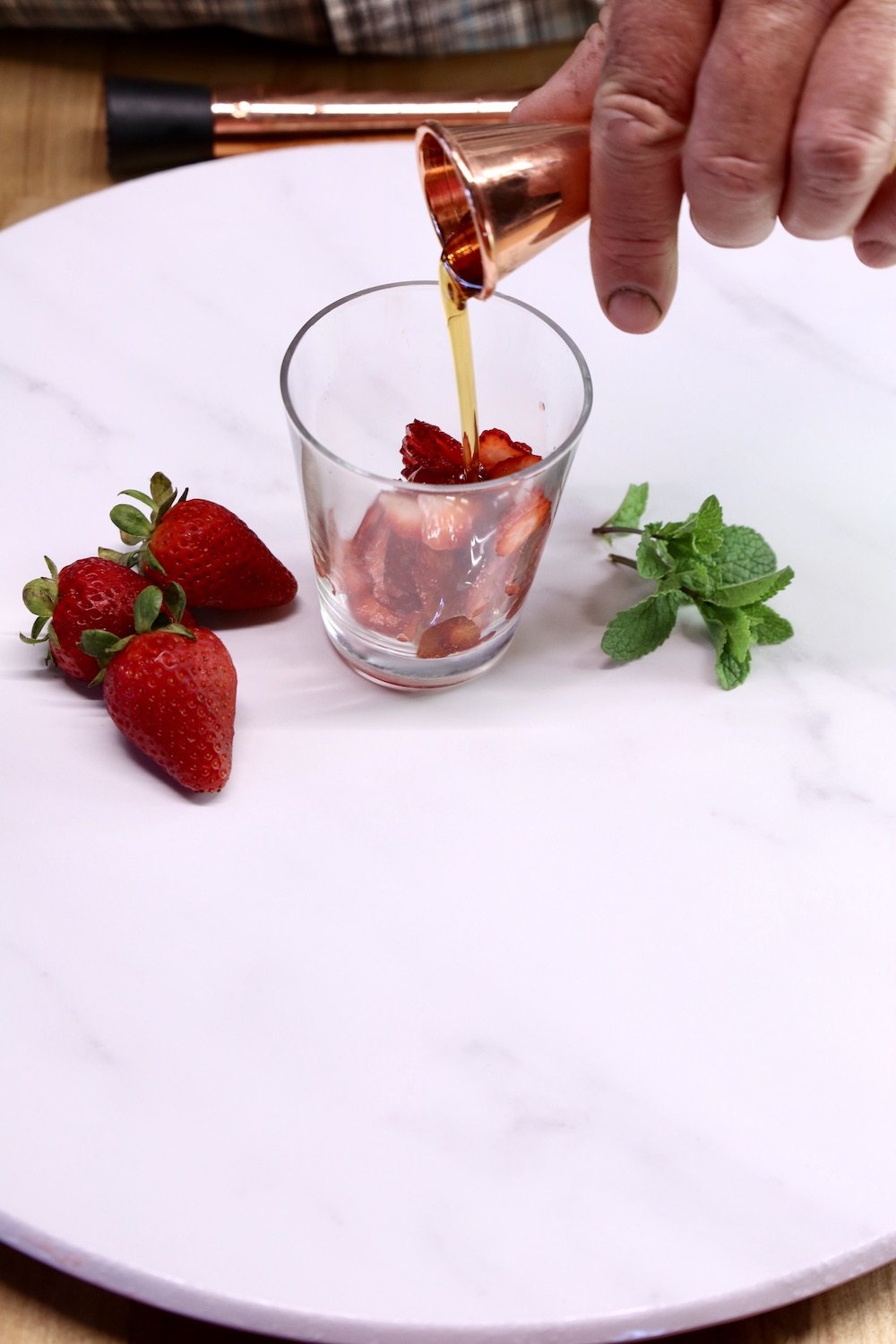 pouring maple syrup into a cocktail glass with a copper jigger
