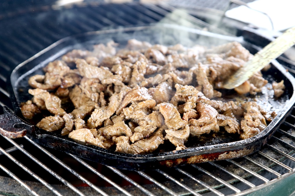 cooking sliced steak on a griddle on a grill for fajitas