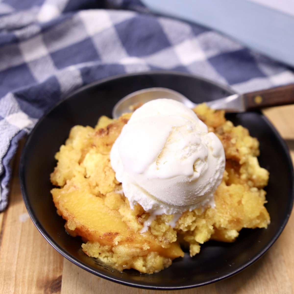 Peach Dump Cake served in a black bowl, topped with vanilla ice cream