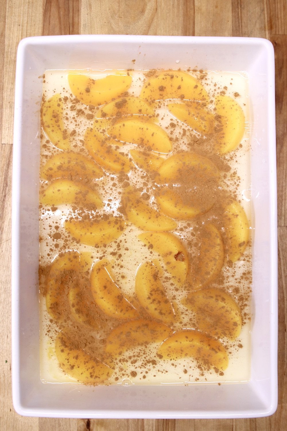 cinnamon sprinkled over sliced peaches in a cake pan